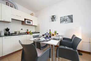 A modern kitchen with white cabinets, a microwave, and a dining area with a table set for four. - Porto Letizia S9 B1, Porlezza, Italy (Porlezza)