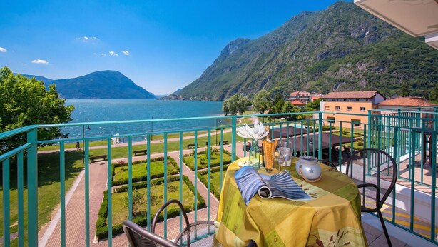 Un balcon avec une table dressée pour le dîner, offrant une vue sur un lac et des montagnes.