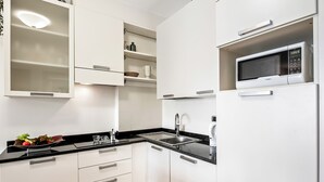 Une cuisine moderne avec des meubles blancs, un plan de travail noir, un four à micro-ondes encastré et un évier en acier inoxydable.