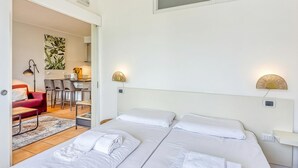 A hotel room with two beds, a red sofa, a dining table with chairs, and a kitchen area.