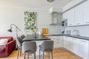 Une cuisine moderne avec des meubles blancs, une table à manger avec des chaises, un canapé rouge et une grande plante.
