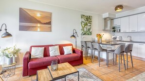 A modern living room with a red sofa, a coffee table, and a kitchen area with a bar and chairs.