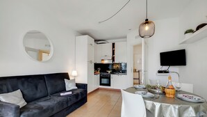 Un saló modern amb un sofà negre, una taula de menjador preparada per a dues persones, i una cuina al fons.