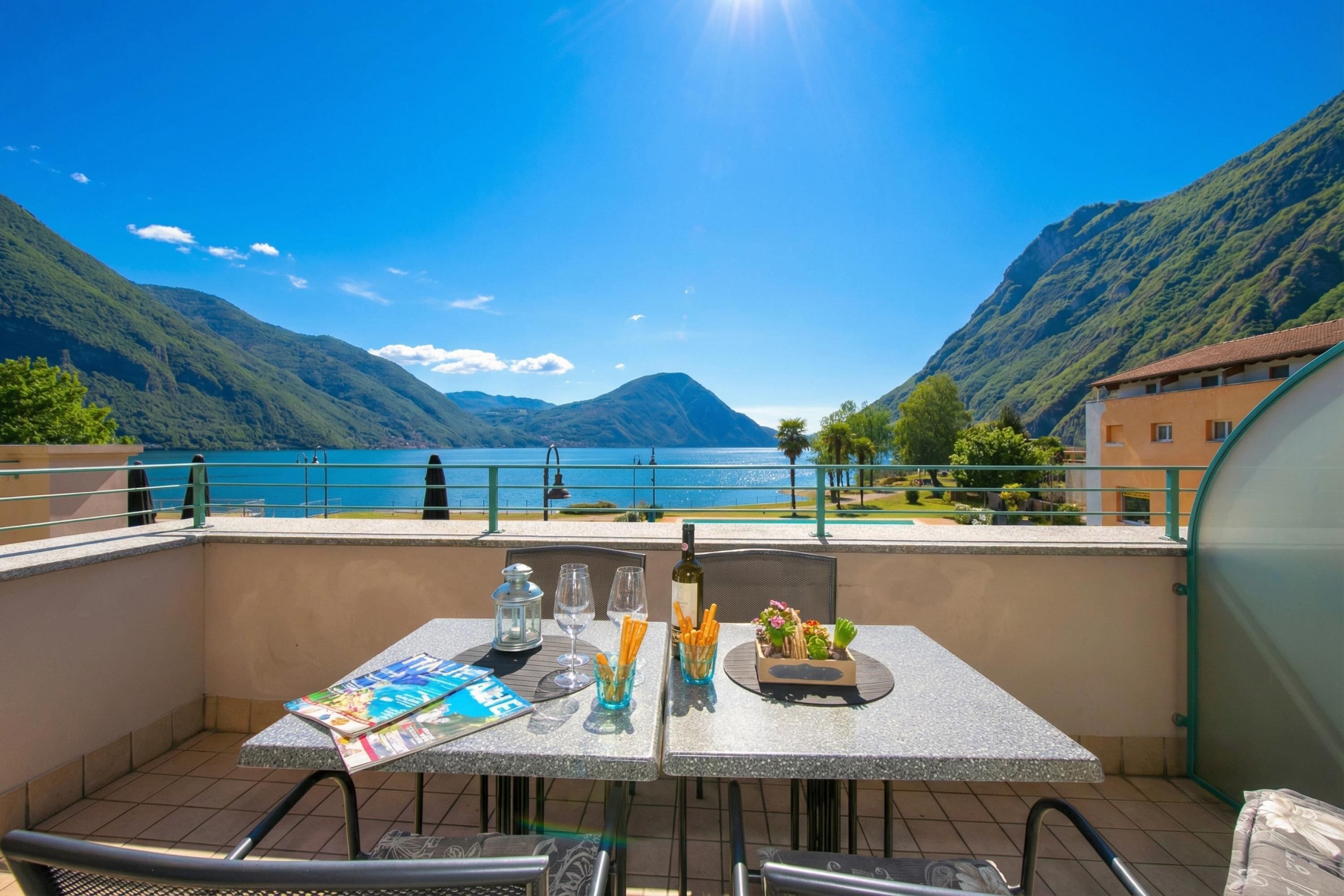 A terrace with a table set for dining, overlooking a lake and mountains.