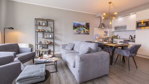 En moderne stue med en grå sofa, et sofabord og en reol. Der er et spiseområde med et træbord og stole.