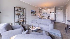 En moderne stue med en grå sofa, et sofabord med magasiner og en reol.