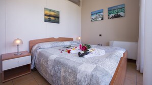 A neatly made bed with a patterned bedspread, a bedside table with a lamp, and two wall-mounted paintings. - Porto Letizia S3 B1, Porlezza, Italy (Porlezza)