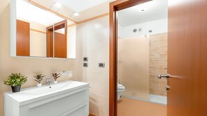 Een moderne badkamer met een grote spiegel, een witte wastafel en een douchecel zichtbaar door een glazen deur.