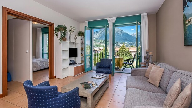 A living room with a sofa, armchair, coffee table, TV, and a balcony with a view of mountains. - Porto Letizia S3 B1, Porlezza, Italy (Porlezza)