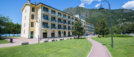 Un hotel de varios pisos con fachada amarilla, un camino pavimentado y montañas al fondo.
