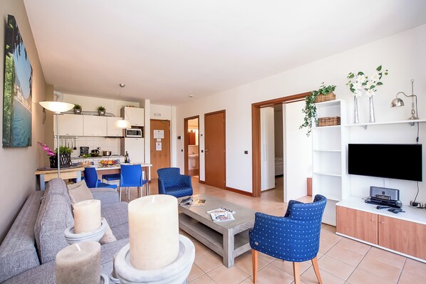 Un salon moderne avec un canapé gris, des fauteuils bleus, une table basse et un téléviseur posé sur un meuble en bois.
