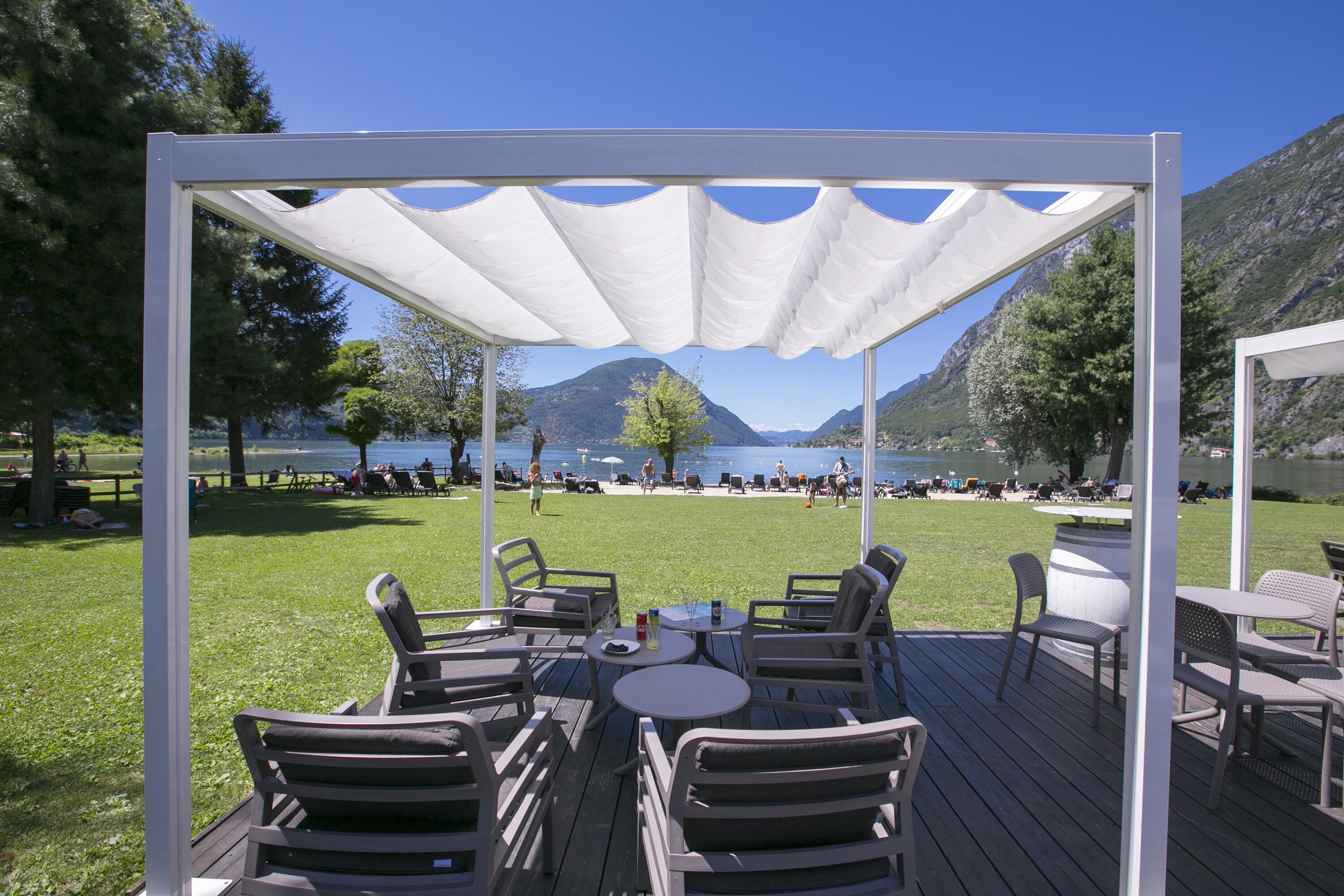Une terrasse en bois avec des sièges extérieurs et un auvent blanc, offrant une vue sur un lac et des montagnes.