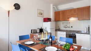 A modern kitchen with wooden cabinets, a microwave, and a stove. There is a dining table set with plates, glasses, and a bottle of wine.
