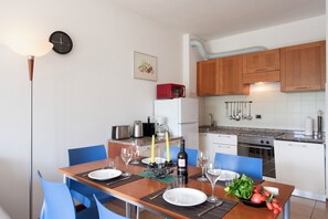 Een eethoek met een tafel gedekt voor twee personen, een magnetron en een koelkast op de achtergrond.