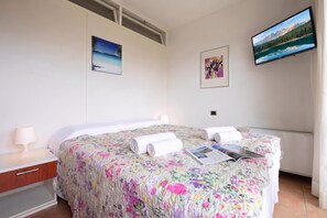 Quarto de hotel com cama, mesa de cabeceira, luminária, televisão e duas fotos emolduradas na parede.