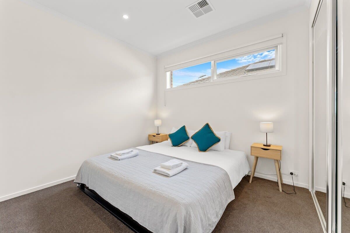 A modern hotel room with a large bed, two bedside tables with lamps, a window with a view, and a carpeted floor.