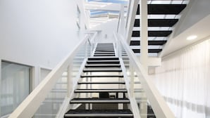 A modern interior with a central staircase flanked by glass railings, leading to a skylight above. - CBD premium location Studio (Adelaide)
