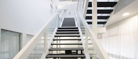 A modern interior with a central staircase flanked by glass railings, leading to a skylight above.