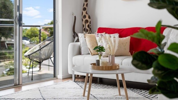 A modern living room with a white sofa, a giraffe sculpture, and a view through a glass door to the outside.