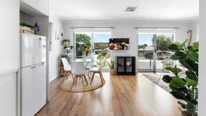 A modern kitchen with white cabinets, a refrigerator, and a dining area with white chairs and a wooden table.
