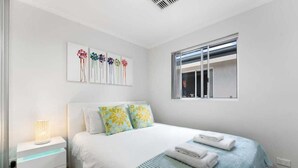 A bedroom with a bed, a nightstand with a lamp, a window, and wall art.