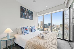 A modern hotel room with a large bed, a city view, and a painting on the wall. - Stylish City Home | Rundle Mall at Your Doorstep (Adelaide)