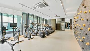 A modern gym with various exercise equipment, large windows, and a unique wall with animal-shaped cutouts.