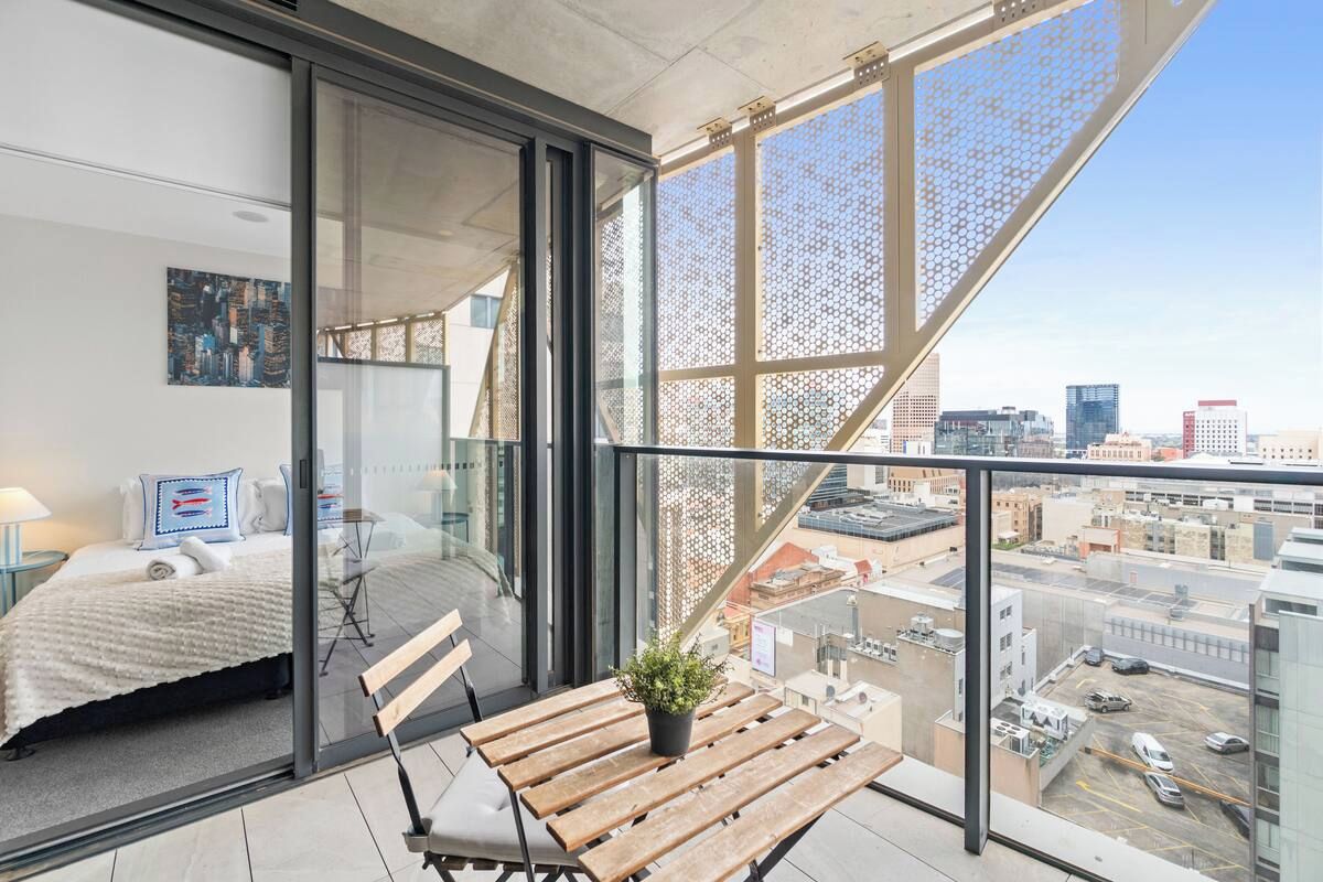 Un balcón con vista a la ciudad, una cama, una mesa de madera y una planta en maceta.