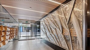 Eine moderne Lobby mit Glastrennwand, Holzregalen und einem großen abstrakten Wandkunstwerk.