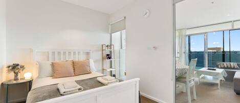 A modern bedroom with a white bed, bedside tables, a mirror, and a view of a balcony with outdoor furniture.