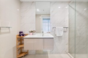 Une salle de bain moderne avec un pare-baignoire en marbre, une douche à parois de verre et une étagère en bois.