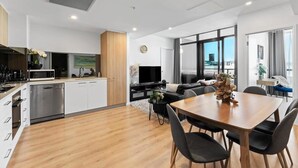 A modern kitchen with white cabinets, a microwave, and a dishwasher. There is a dining area with a wooden table and black chairs.