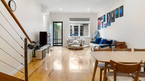 A modern living room with a wooden staircase, a sofa set, a dining table, and a TV. - Lego-Aerospace/Free Parking/CBD/Chinatown (Adelaide)