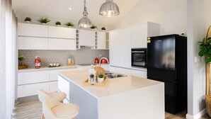 Een moderne keuken met witte kasten, een centraal eiland, hangende lampen en een zwarte koelkast.