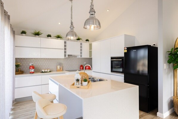 A modern kitchen with white cabinetry, a central island, pendant lighting, and a black refrigerator. - An Idyllic Boho Style Retreat,High-end kitchenware (Mermaid Waters)
