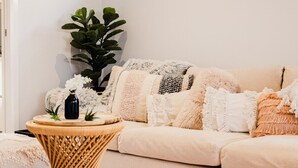 Een gezellige woonkamer met een beige bank, een rond houten bijzettafeltje en een grote groene plant.