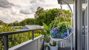 Een balkon met een hangstoel, potplanten en uitzicht op groen en huizen.