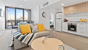 Un appartement moderne comprenant un salon, un coin repas et une cuisine. Une grande fenêtre offre une vue sur la ville.