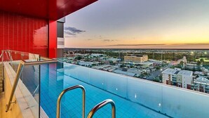 Une piscine à débordement située sur le toit, offrant une vue sur la ville au coucher du soleil.