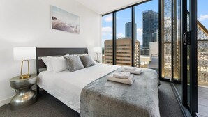 Una habitación de hotel moderna con una cama grande, vistas a la ciudad y un balcón con barandilla de malla.