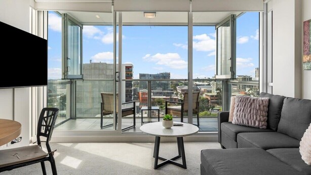 Een moderne woonkamer met een groot balkon, een bank, een eettafel en stoelen.