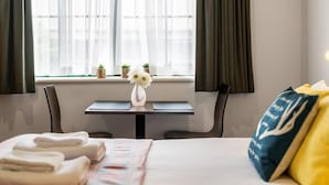 Een hotelkamer met een bed, een nachtkastje met een bloevas, een raam met gordijnen en uitzicht op de stad.