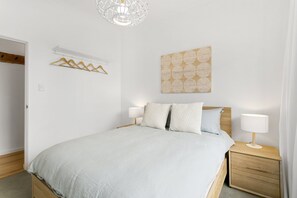 A bedroom with a bed, bedside tables, a hanging light fixture, and a wall art piece.
