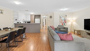 Ein modernes Wohnzimmer mit grauem Sofa, einem Esstisch mit Stühlen, einer Küchenzeile und einem Fernseher.