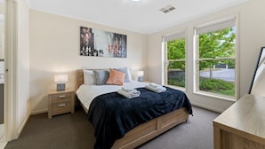 Ein Schlafzimmer mit einem Bett, Nachttischen, einem Gemälde und einem großen Fenster mit Blick auf Grünflächen.