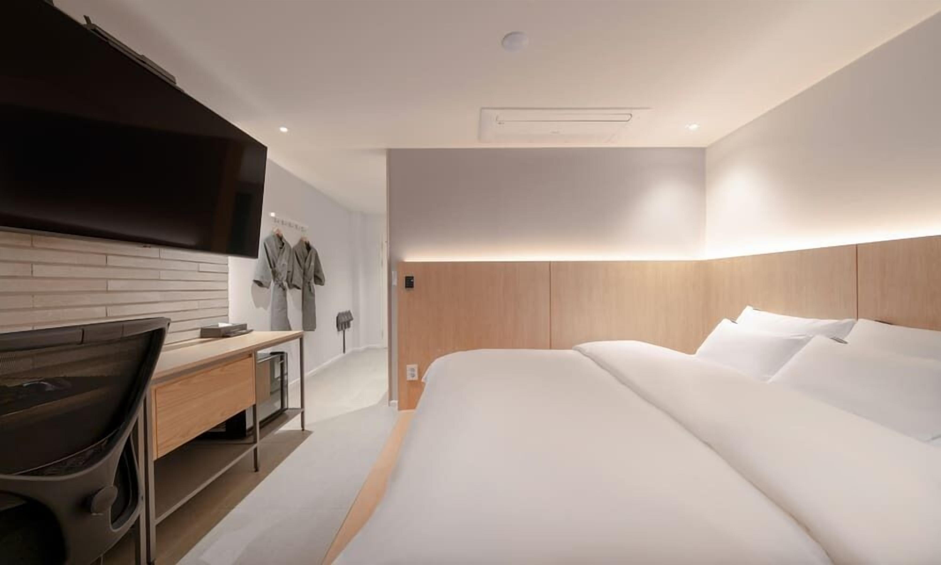A modern hotel room with a large bed, a desk with a chair, a flat-screen TV, and a wooden headboard.