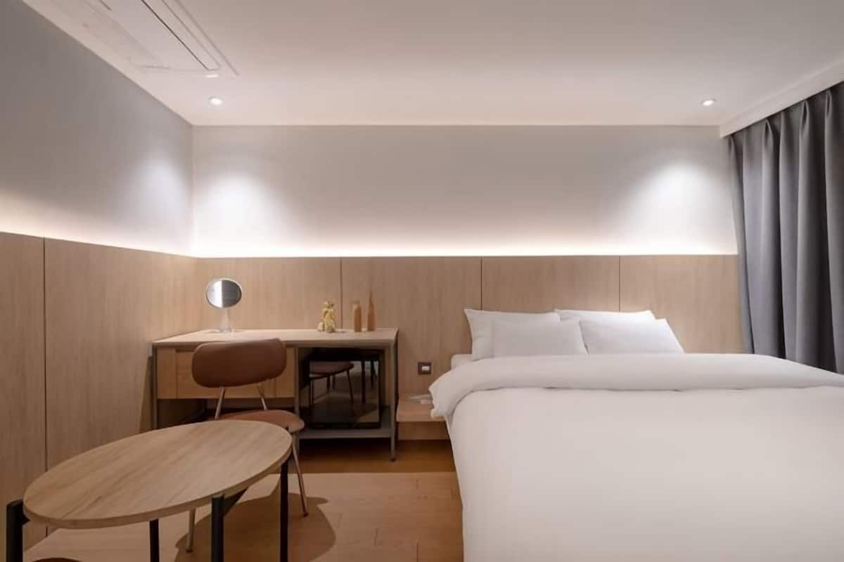A hotel room with a bed, desk, chair, and a small table.
