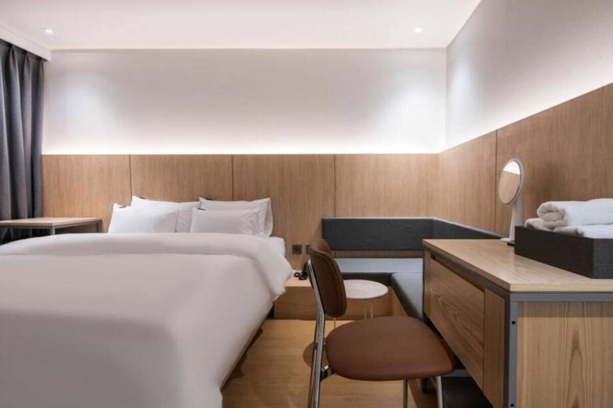 Een moderne hotelkamer met een groot bed, een bureau, een stoel, een ronde spiegel en een klein rond tafeltje.