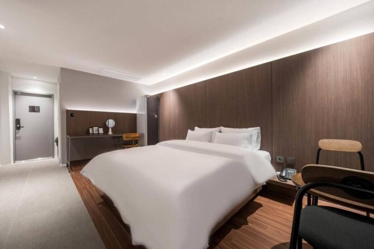 Een moderne hotelkamer met een groot bed, een bureau, een stoel en een bijzettafeltje met een lamp.