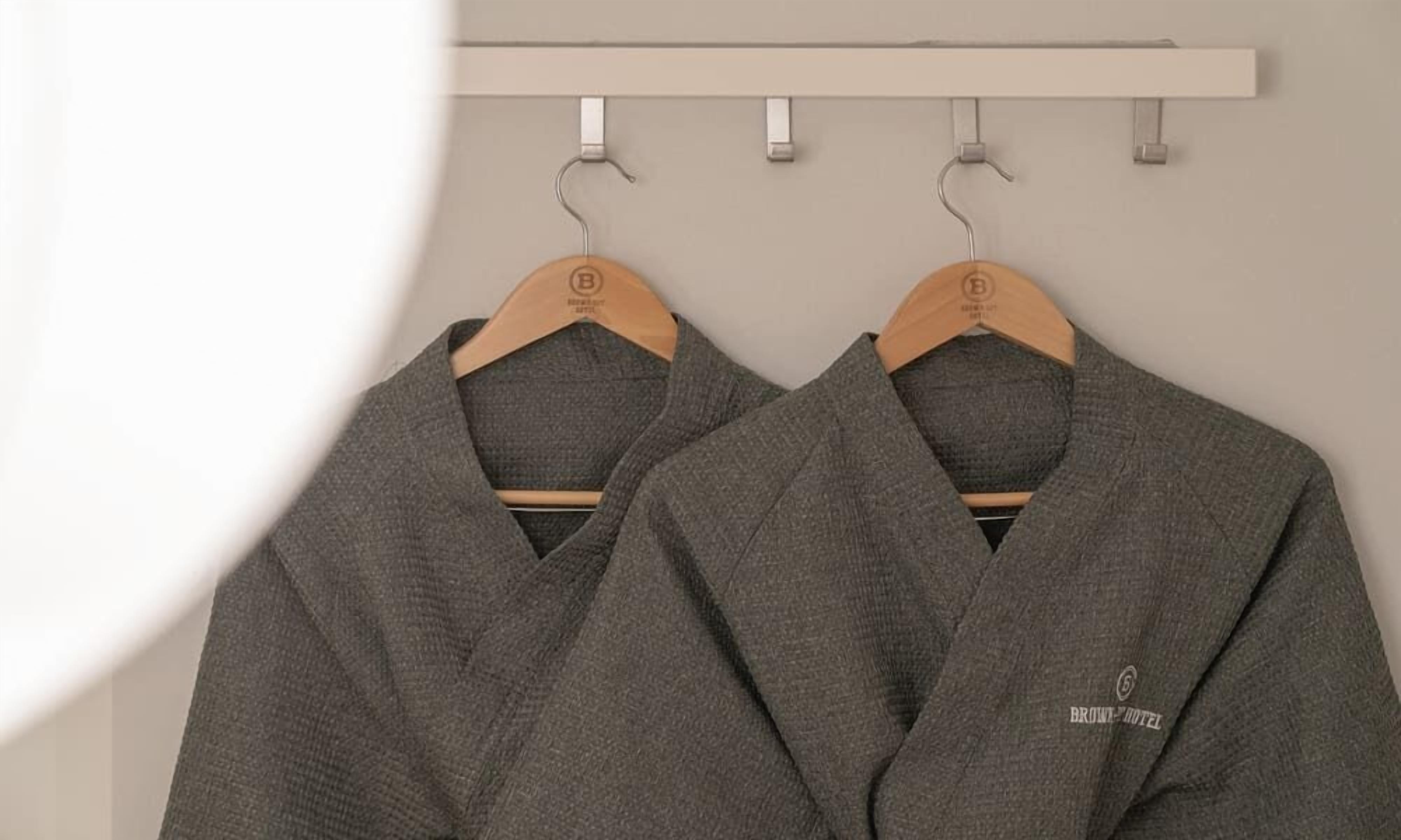 Two grey robes hanging on a wooden rack against a plain wall.